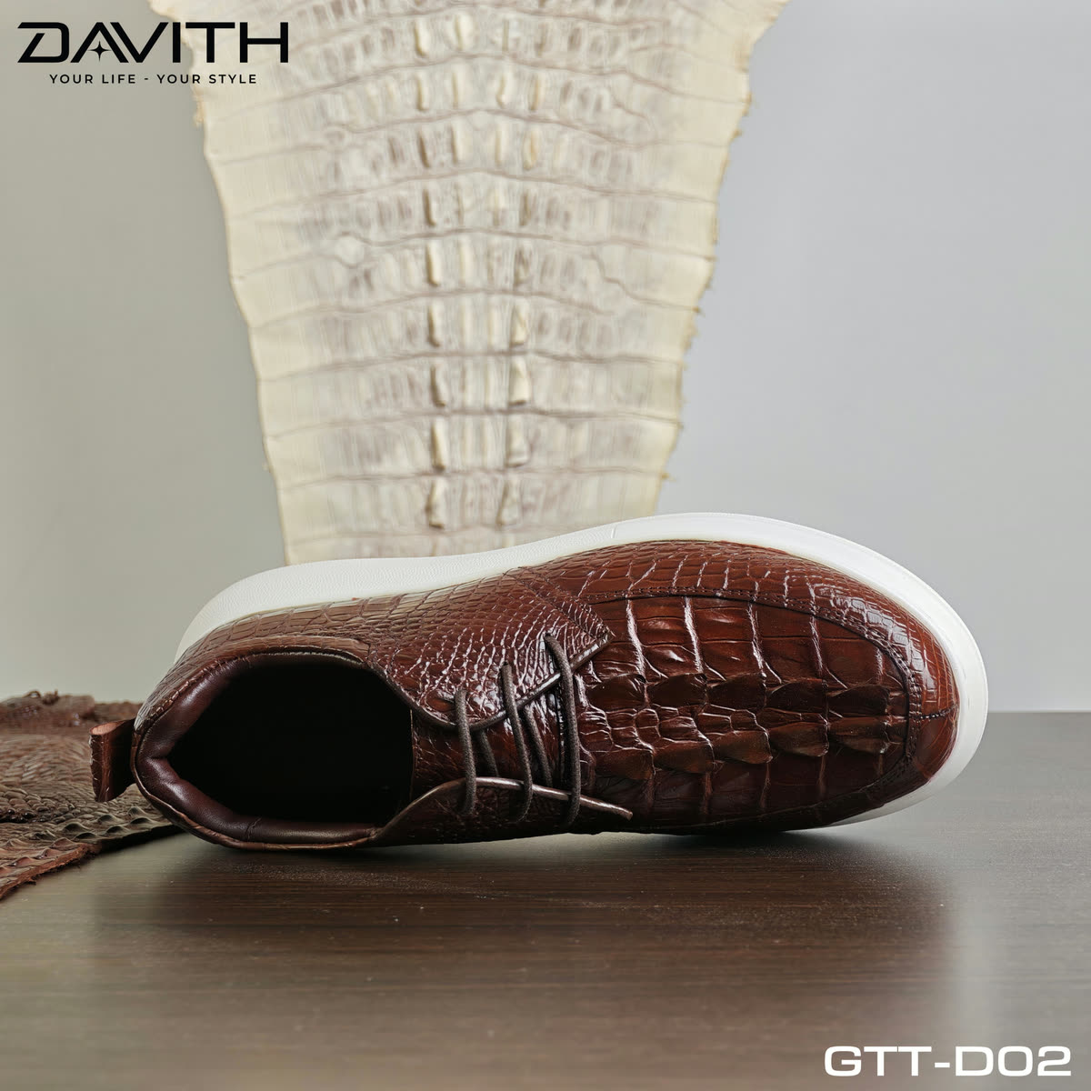 Đôi sneaker GTT-D02 nâu cognac đặt trước tấm da cá sấu